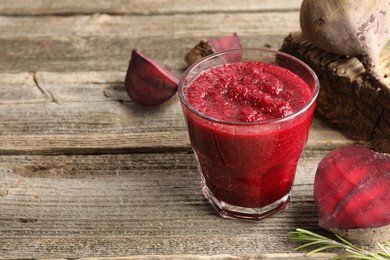 Photo of Fresh beetroot smoothie in glass, rosemary and cut vegetables on wooden table, closeup. Space for text