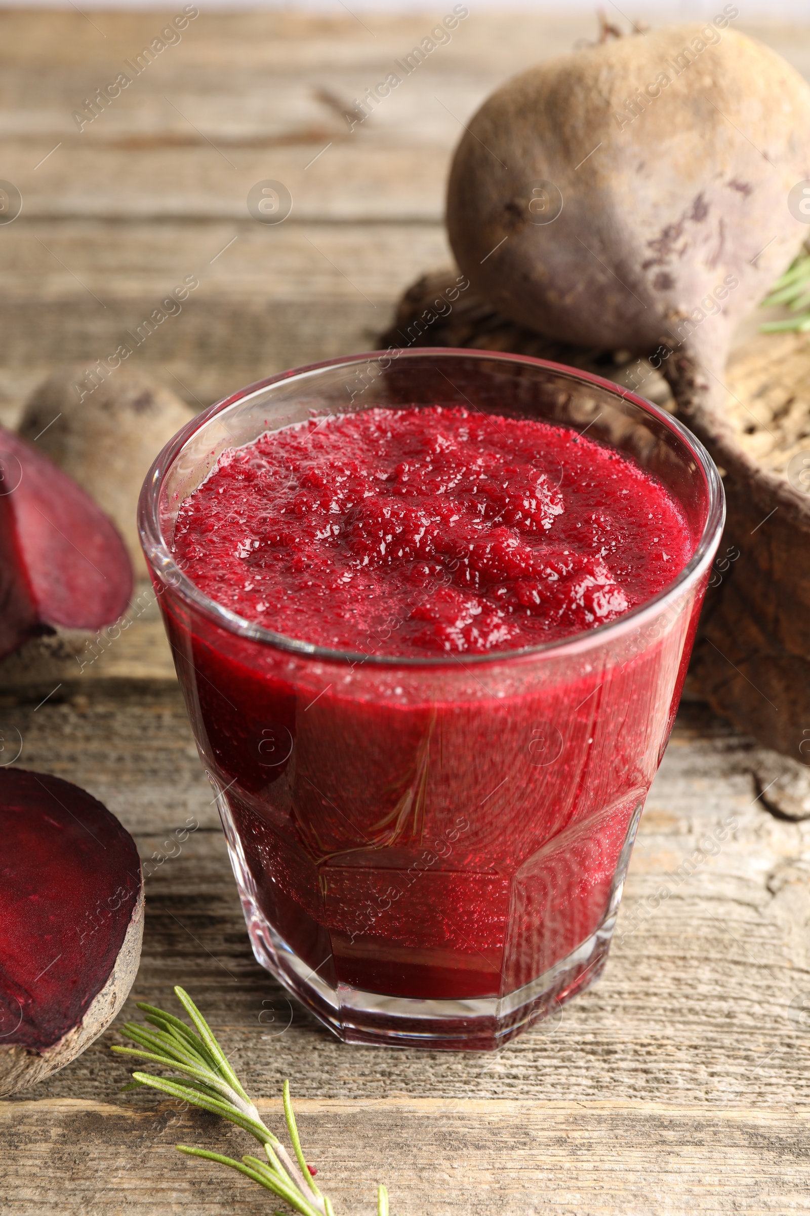 Photo of Fresh beetroot smoothie in glass, rosemary and cut vegetables on wooden table, closeup