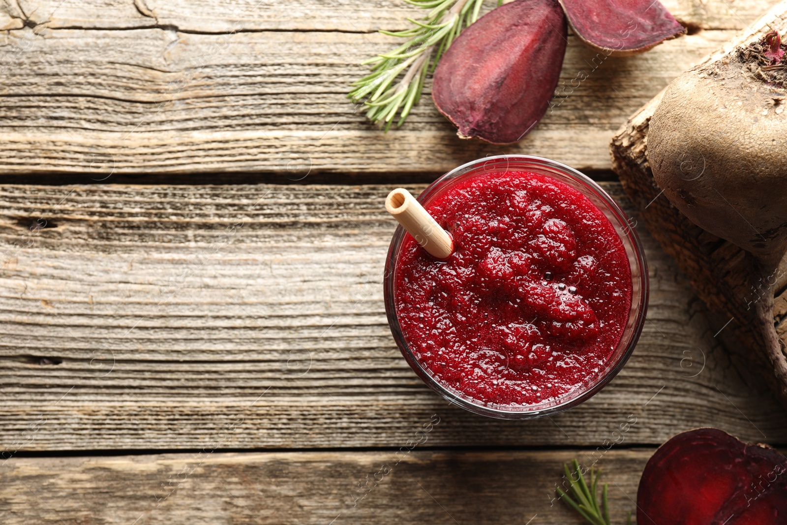 Photo of Fresh beetroot smoothie in glass, rosemary and cut vegetable on wooden table, flat lay. Space for text