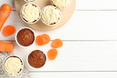 Photo of Tasty carrot muffins and fresh vegetables on white wooden table, flat lay. Space for text