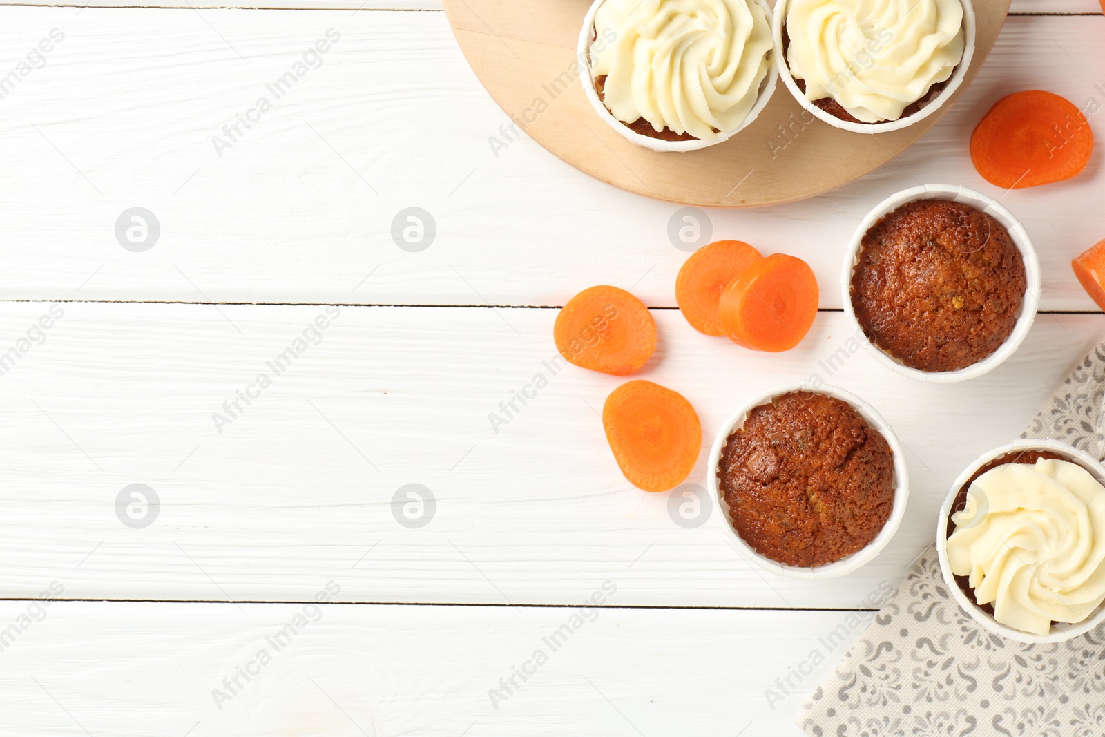 Photo of Tasty carrot muffins and fresh vegetable on white wooden table, flat lay. Space for text