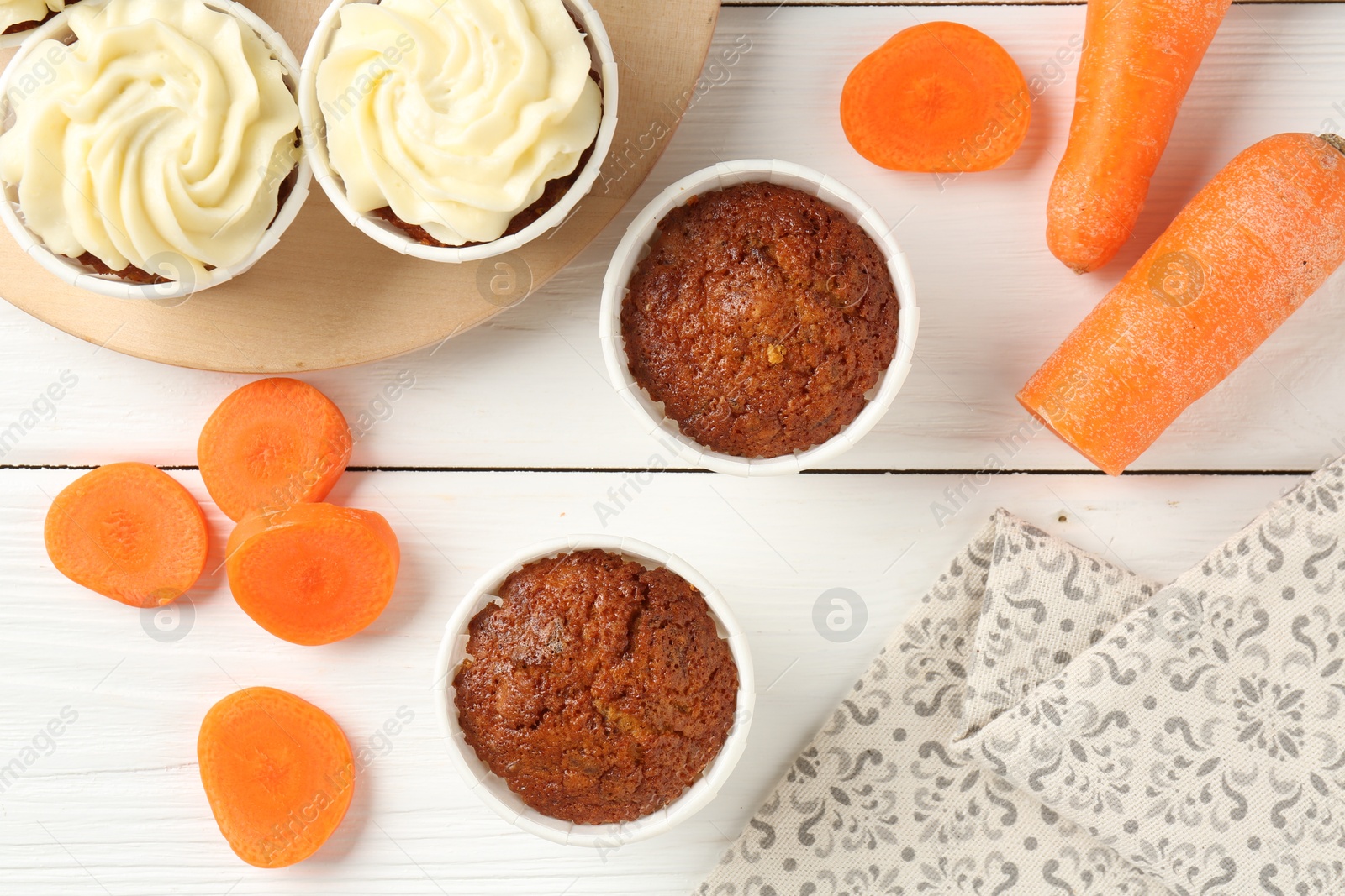 Photo of Tasty carrot muffins and fresh vegetables on white wooden table, flat lay