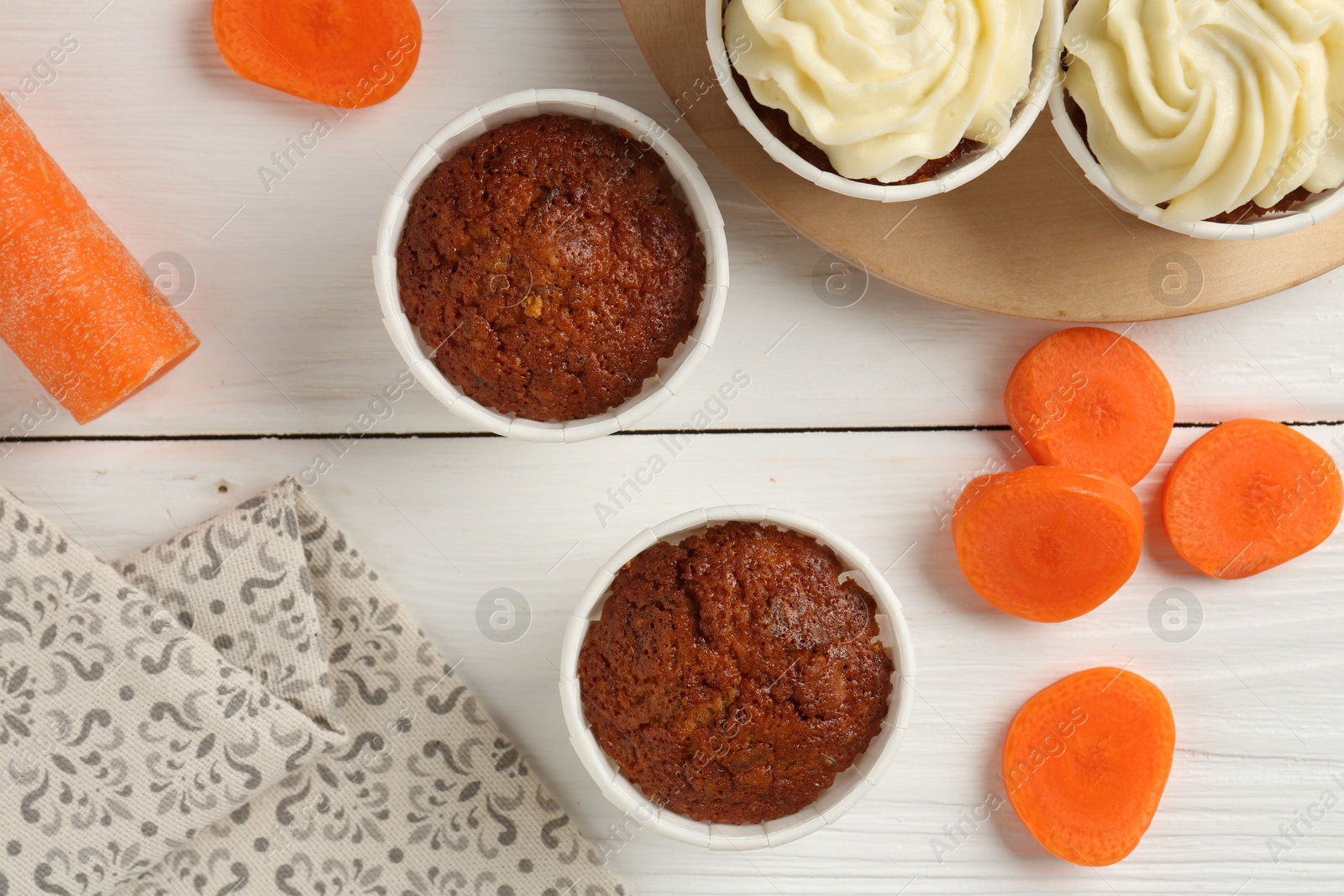 Photo of Tasty carrot muffins with cream and fresh vegetable on white wooden table, flat lay