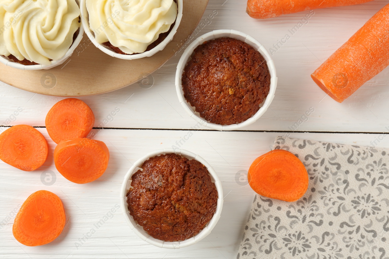 Photo of Tasty carrot muffins and fresh vegetables on white wooden table, flat lay