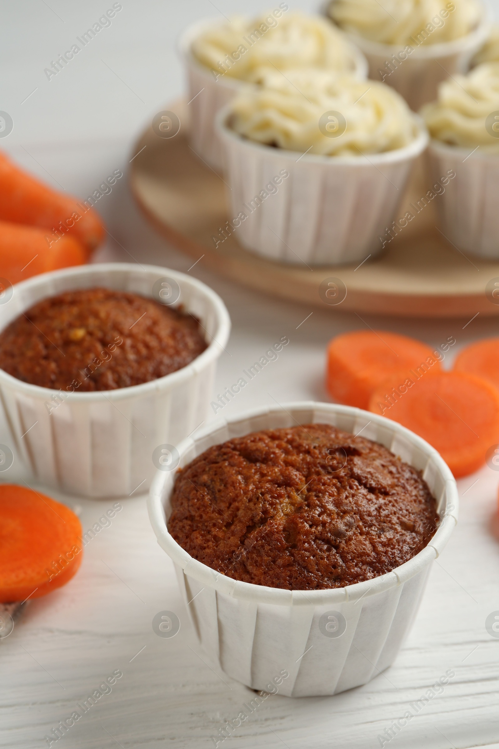 Photo of Tasty carrot muffins with cream and fresh vegetable on white wooden table, closeup