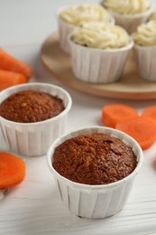 Photo of Tasty carrot muffins with cream and fresh vegetable on white wooden table, closeup