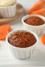 Photo of Tasty carrot muffins with cream and fresh vegetable on white wooden table, closeup