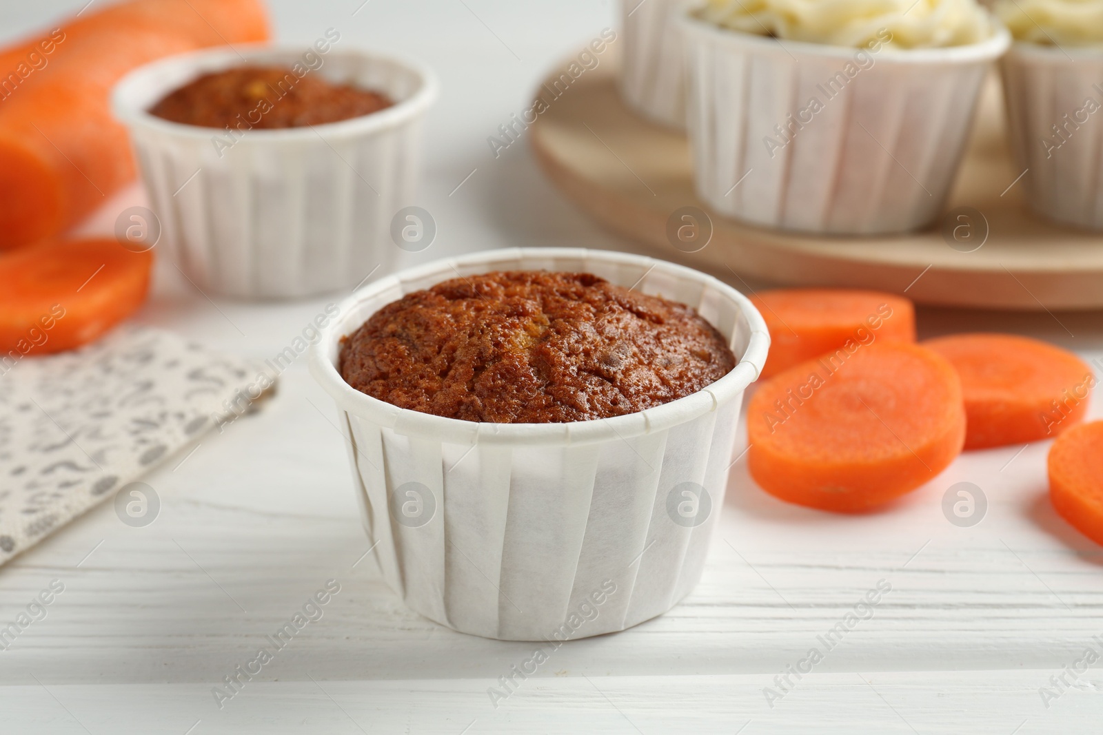 Photo of Tasty carrot muffins with cream and fresh vegetable on white wooden table, closeup