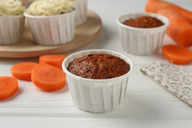 Photo of Tasty carrot muffins with cream and fresh vegetables on white wooden table, closeup