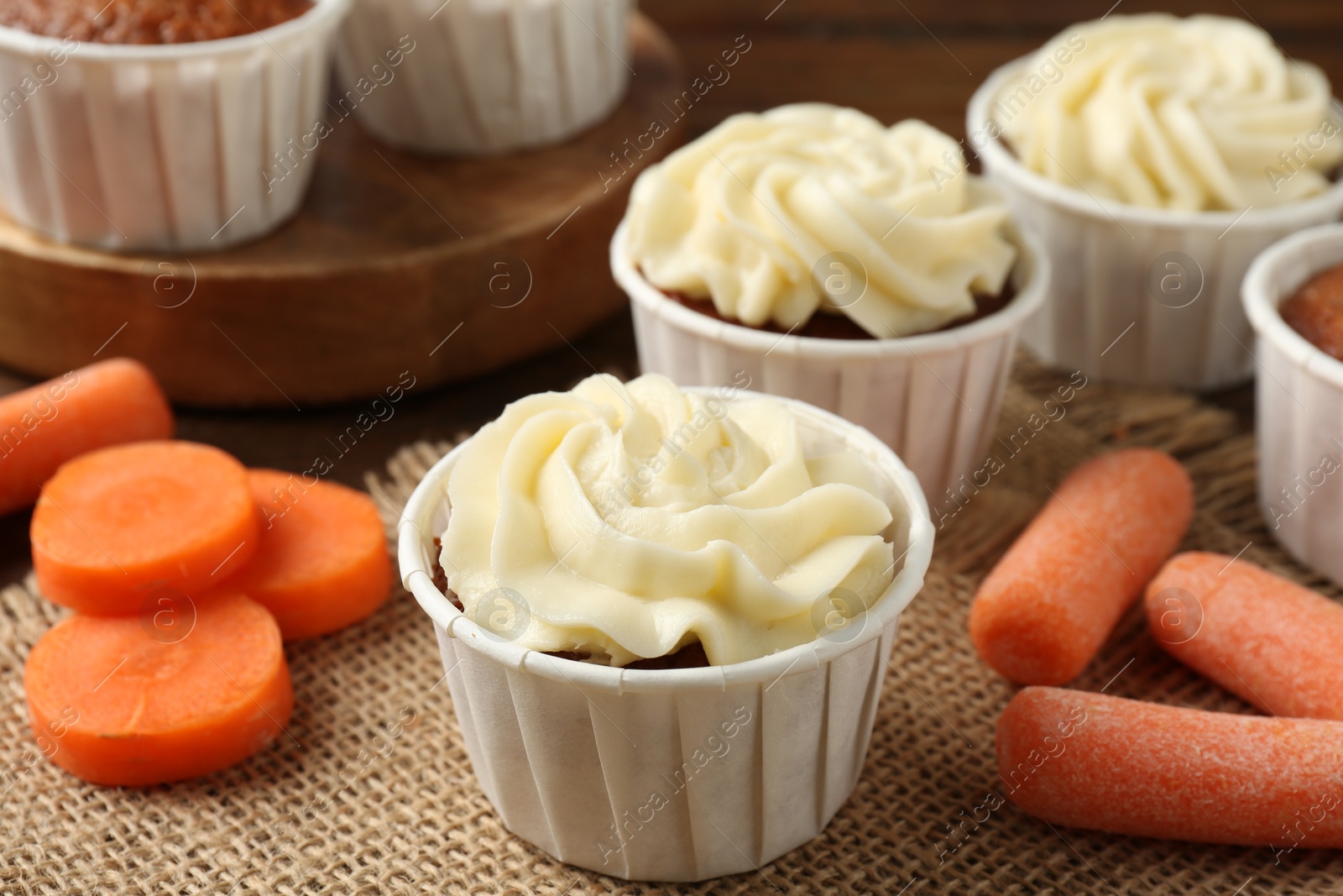 Photo of Tasty carrot muffins with cream and fresh vegetables on table, closeup