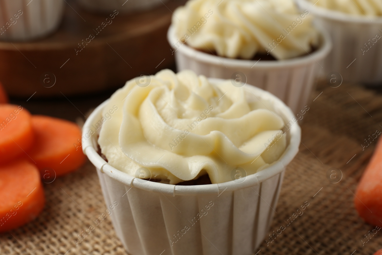 Photo of Tasty carrot muffins with cream and fresh vegetable on table, closeup