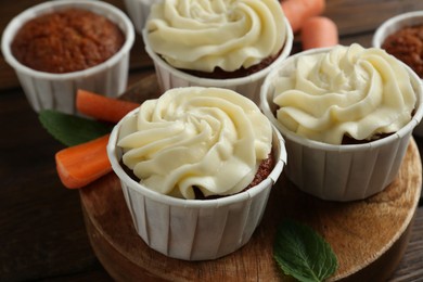 Photo of Tasty carrot muffins and fresh vegetable on wooden table, closeup