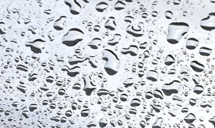 Water drops on light grey glass surface, closeup