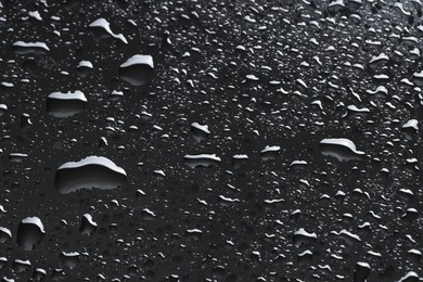 Photo of Water drops on dark grey glass surface, closeup