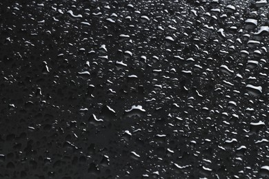 Photo of Water drops on dark grey glass surface, closeup