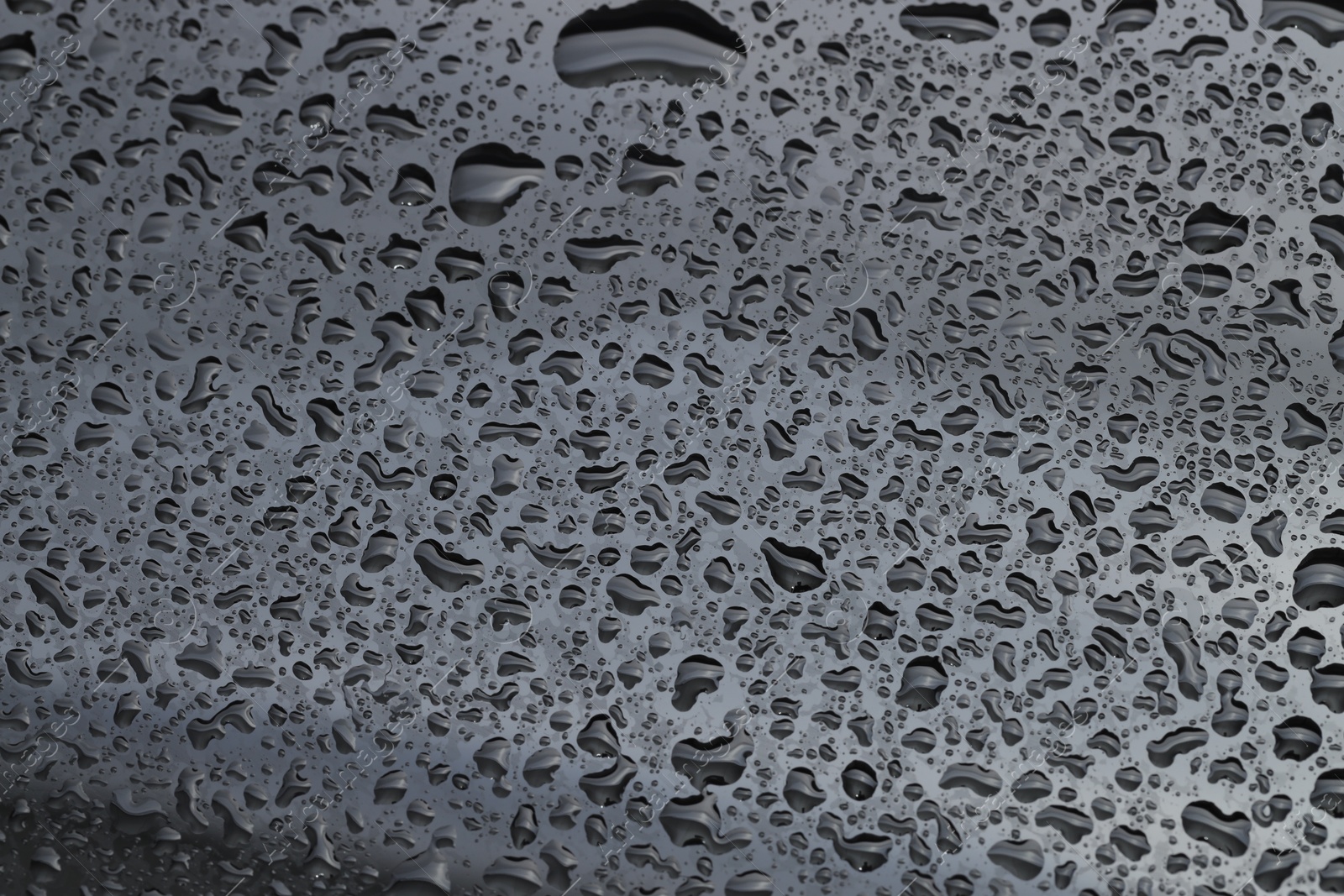 Photo of Water drops on dark grey glass surface, top view