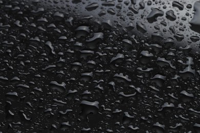 Photo of Water drops on black glass surface, closeup