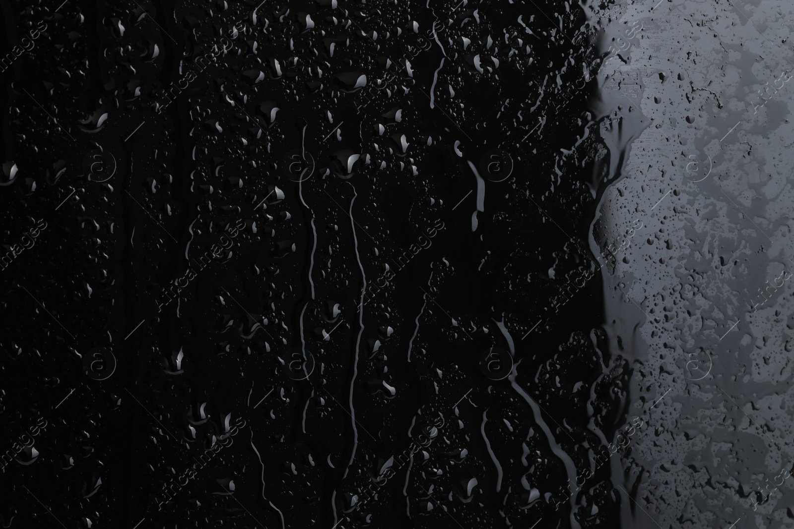 Photo of Water drops on black glass surface, closeup