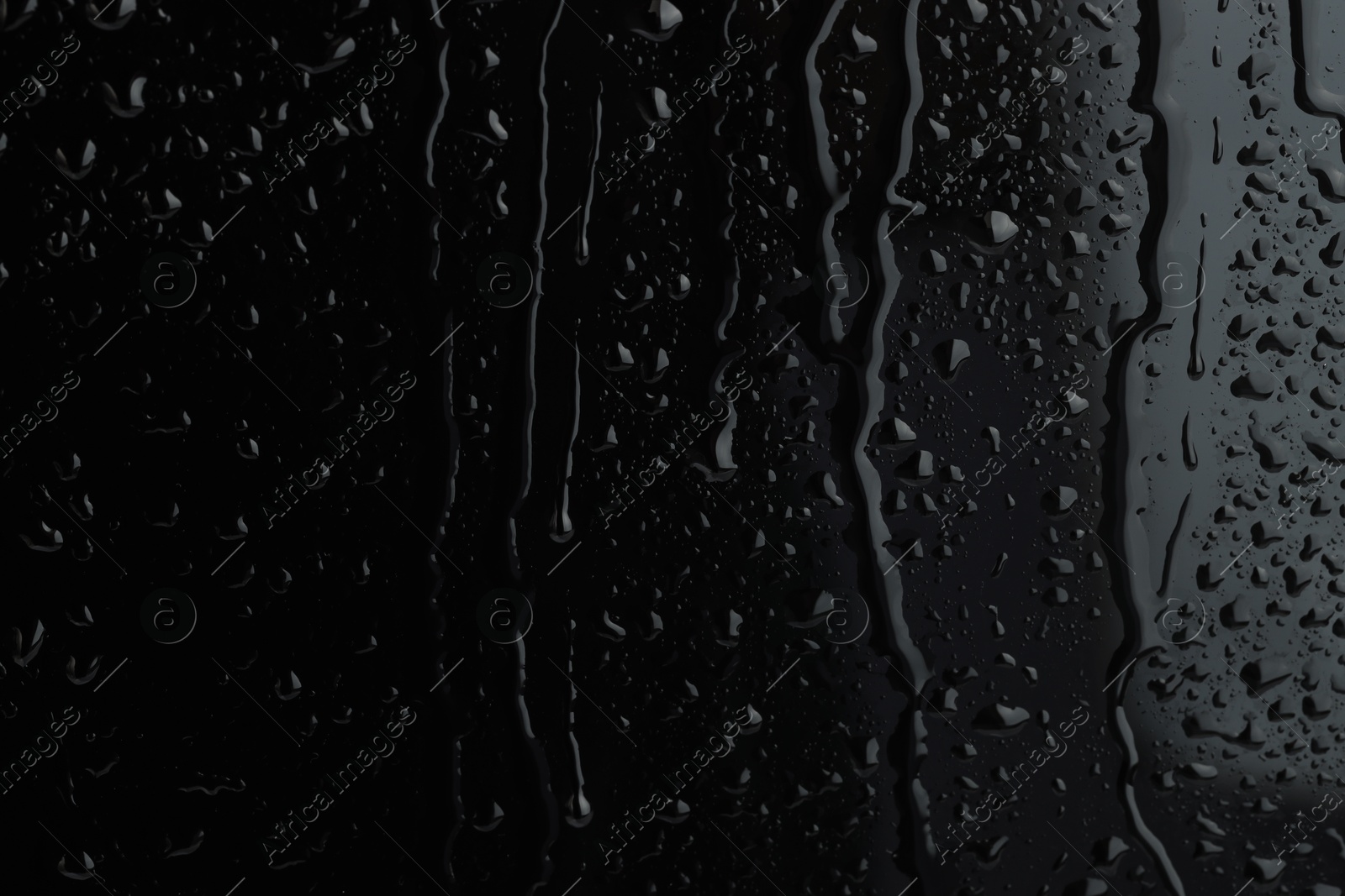 Photo of Water drops on black glass surface, closeup