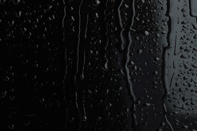 Photo of Water drops on black glass surface, closeup