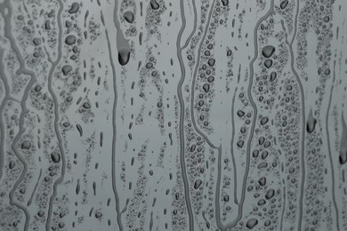 Photo of Water drops on grey glass surface, closeup