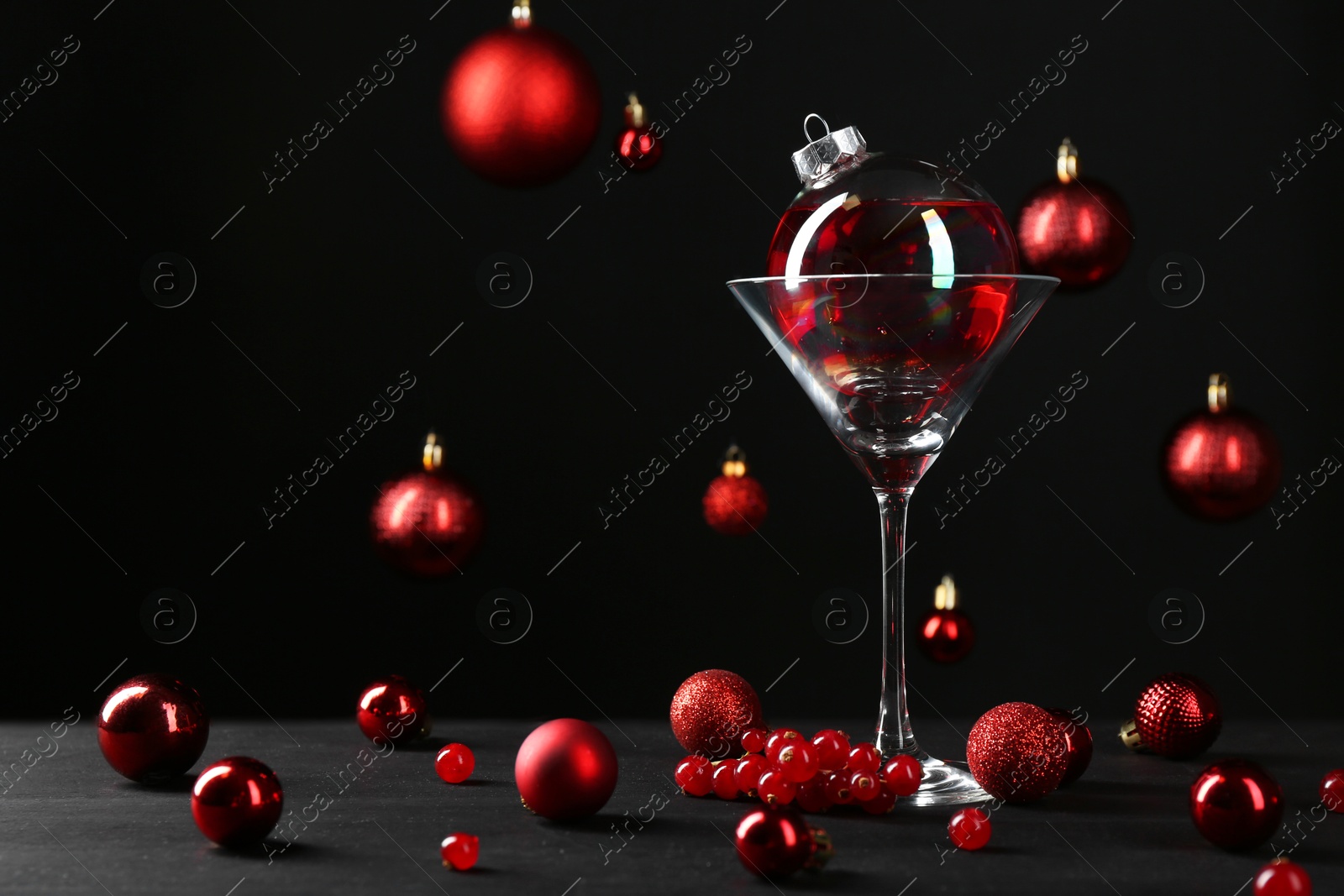 Photo of Creative presentation of Christmas cocktail in bauble and glass on black table