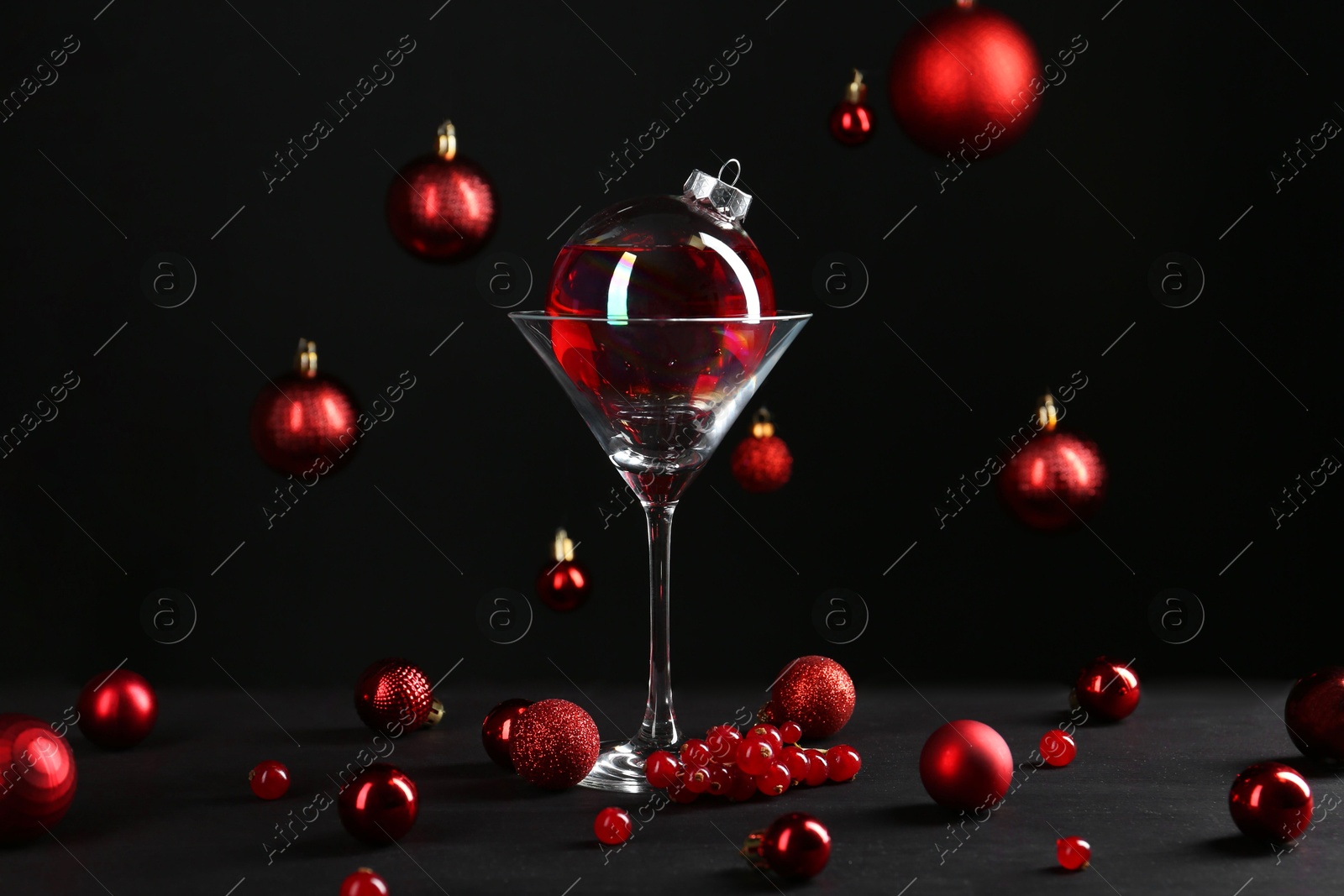 Photo of Creative presentation of Christmas cocktail in bauble and glass on black table