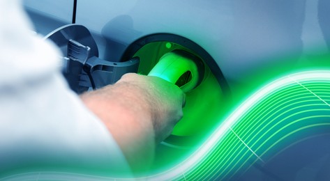 Image of Man inserting plug into electric car socket at charging station outdoors, closeup. Banner design. Waves representing energy