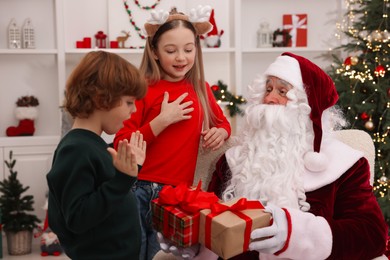 Photo of Christmas celebration. Santa Claus giving gift boxes to emotional kids at home