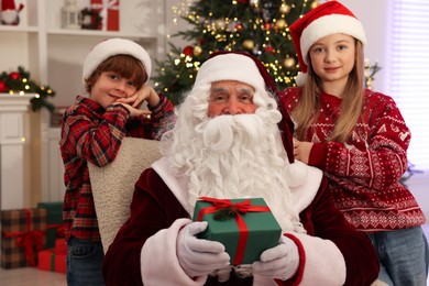 Photo of Christmas celebration. Santa Claus with kids and gift box at home