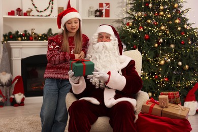 Christmas celebration. Santa Claus giving gift box to girl at home