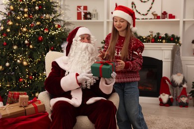 Photo of Christmas celebration. Santa Claus giving gift box to girl at home