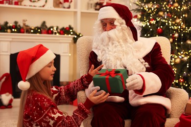 Christmas celebration. Santa Claus giving gift box to girl at home