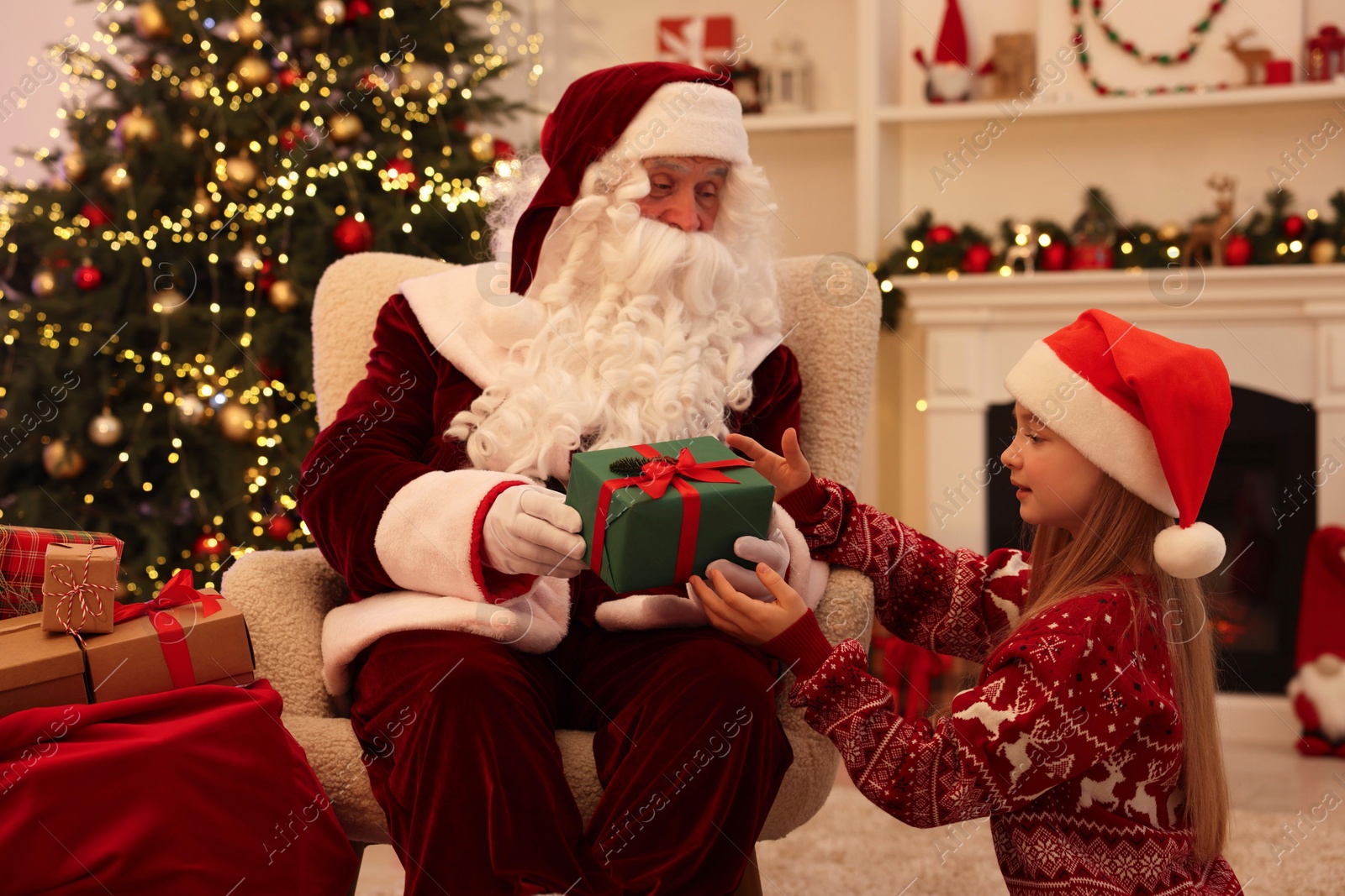 Photo of Christmas celebration. Santa Claus giving gift box to girl at home