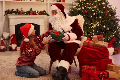 Photo of Christmas celebration. Santa Claus giving gift box to girl at home