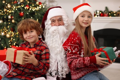 Photo of Christmas celebration. Santa Claus and kids with gift boxes at home