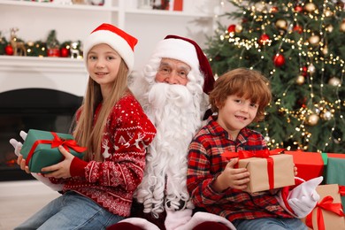 Photo of Christmas celebration. Santa Claus and kids with gift boxes at home