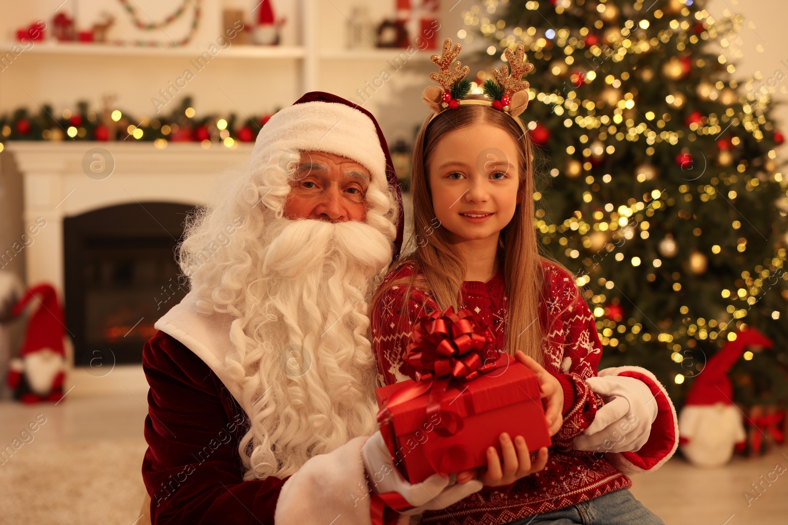 Photo of Christmas celebration. Santa Claus giving gift box to girl at home