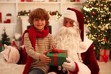 Photo of Christmas celebration. Santa Claus and boy with gift box at home