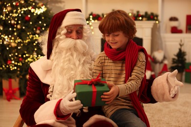 Photo of Christmas celebration. Santa Claus and boy with gift box at home