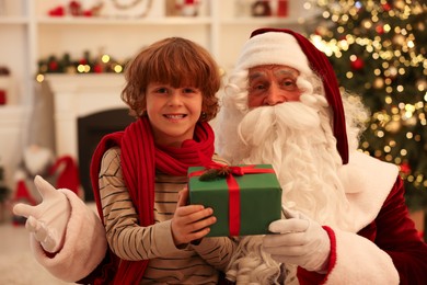 Photo of Christmas celebration. Santa Claus and boy with gift box at home