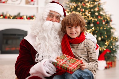 Photo of Christmas celebration. Santa Claus and boy with gift box at home