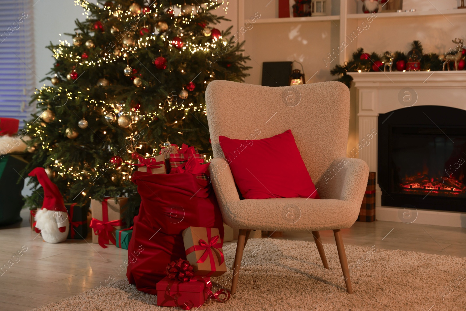 Photo of Bag with gift boxes, armchair and Christmas tree near decorated fireplace in room. Festive interior