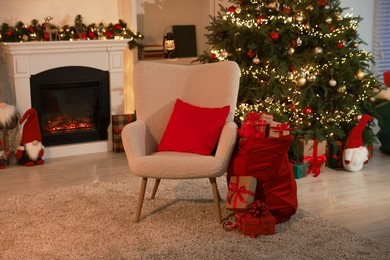 Photo of Bag with gift boxes, armchair and Christmas tree near decorated fireplace in room. Festive interior