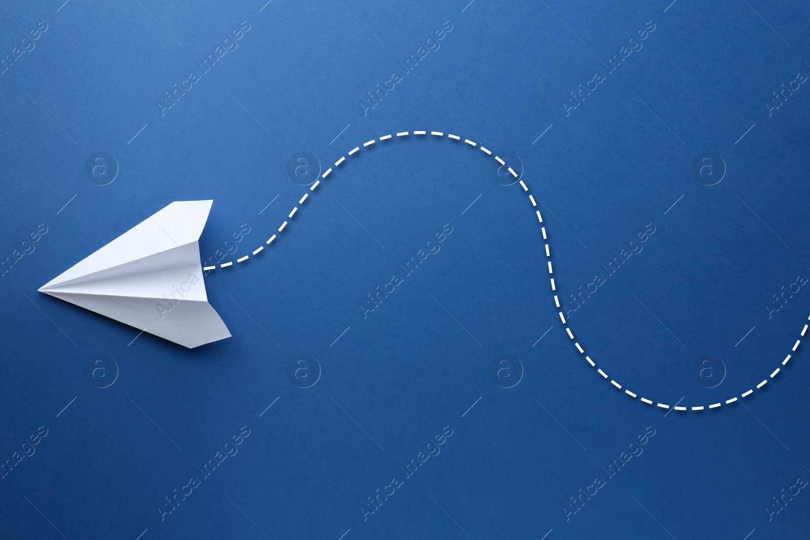 Image of White paper plane with flight path on blue background. Dashed line for trajectory