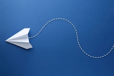 Image of White paper plane with flight path on blue background. Dashed line for trajectory