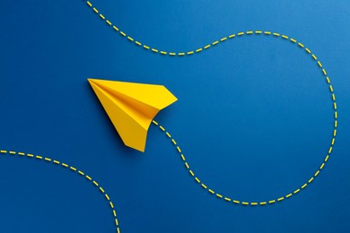 Image of Yellow paper plane with flight path on blue background. Dashed line for trajectory