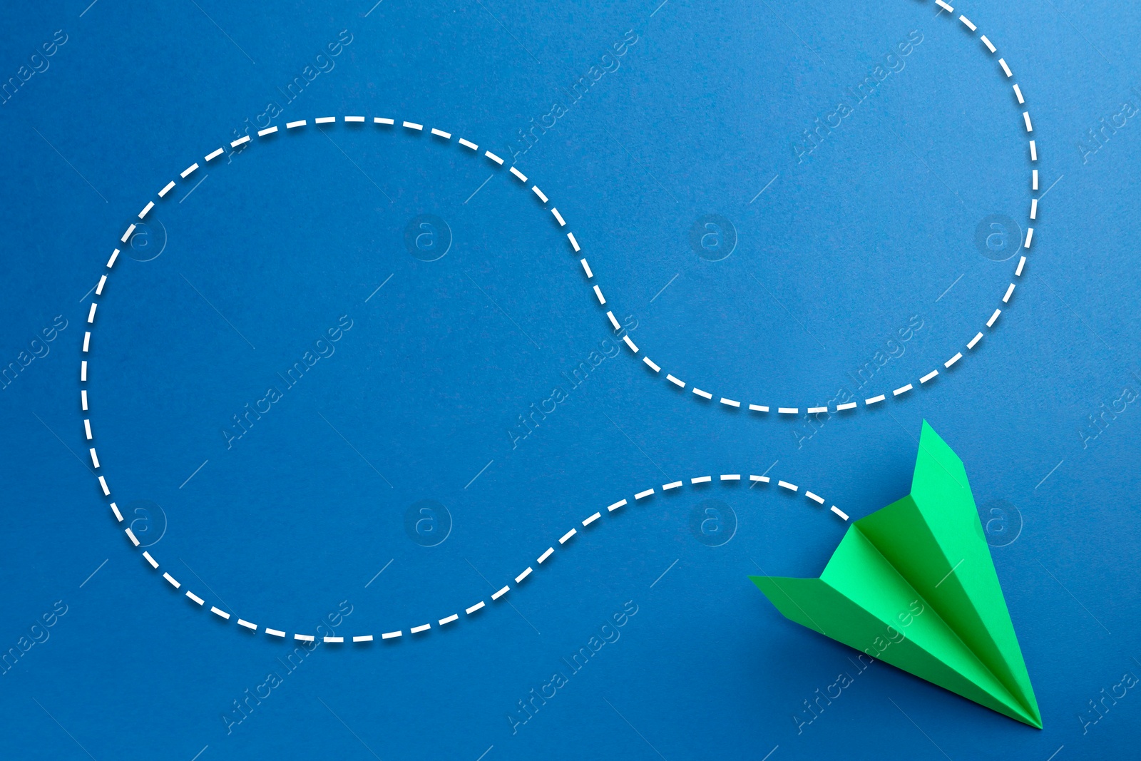 Image of Green paper plane with flight path on blue background. Dashed line for trajectory