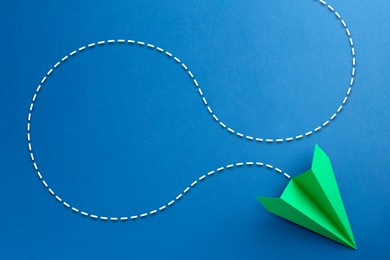 Image of Green paper plane with flight path on blue background. Dashed line for trajectory