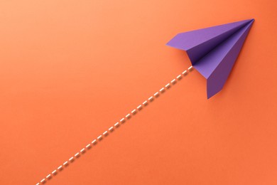 Image of Purple paper plane with flight path on orange background. Dashed line for trajectory